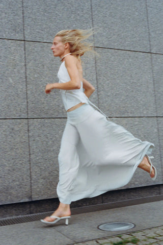 Woman in a white outfit running on a sidewalk with a gray wall in the background